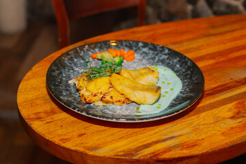 Fried fish fillet with vegetables and sauce on a beautiful plate on a wooden table in a restaurant
