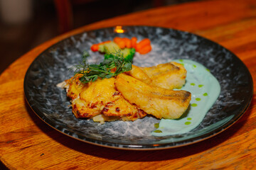 Fried fish fillet with vegetables and sauce on a beautiful plate on a wooden table in a restaurant. dishes from the menu