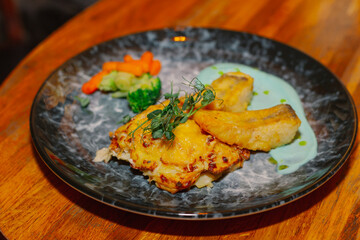 Fried fish fillet with vegetables and sauce on a beautiful plate on a wooden table in a restaurant. dishes from the menu. new cooking recipe