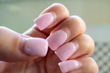 A close-up of a hand with an outgrown acrylic or gel manicure in a soft pink shade