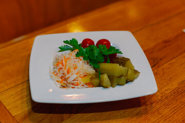 Pickled cabbage cucumbers tomatoes on one white plate with herbs on a wooden table