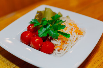 Pickled cabbage cucumbers tomatoes on one white plate with herbs on a wooden table. appetizer for vodka. close-up