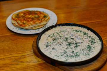 Fresh fried pancakes on a plate and gravy in a pan with sour cream herbs and mushrooms