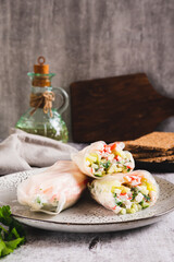 Spring rolls in rice paper with crab sticks, cucumber, greens and sauce on a plate on vertical view