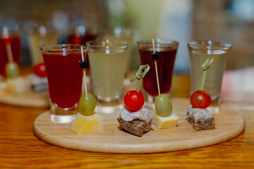 Alcoholic liqueur in shots of different types with a snack on a wooden stand on a bar counter in a...