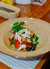 A beautiful salad of fresh vegetables with sour cream and greens on a plate on a wooden table in a restaurant. vertical frame
