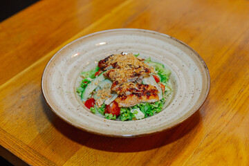 Fresh salad of vegetables with pieces of chicken grilled upstairs in a plate on a wooden table in a cafe