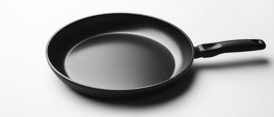 Empty black frying pan with a long handle sits on a white surface