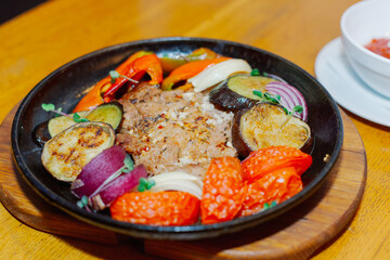 A variety of baked vegetables along with fried pork in a pan with sauce. Beautiful feed in a restaurant. close-up