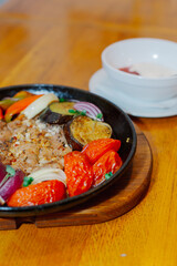 A variety of baked vegetables along with fried pork in a pan with sauce. Beautiful feed in a restaurant. Vertical plan