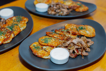 Plates with fried pancakes of potatoes fried meat with onions and sauce on a wooden table. The kitchen of the whole world