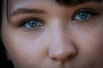 Fototapeta premium Close-up portrait of a woman with striking blue eyes and natural makeup, partially obscured by strands of dark hair blowing across her face.