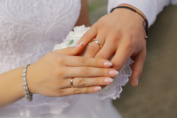Beautiful hands of newlyweds with engagement rings lie on each other under them a wedding bouquet