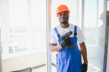 African handyman adjusting white pvc plastic window indoors. worker using screwdriver to repair upvc window.