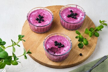 Berry dessert, yogurt mousse or jelly with blueberries in glass bowls on a wooden board on a light concrete background. No-bake desserts.