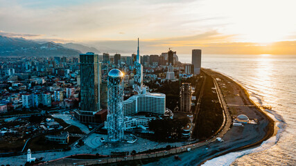 Obraz premium Batumi cityscape from above, revealing modern architecture, iconic alphabetic tower, coastal scenery, and caucasus mountain backdrop under glowing sunset light