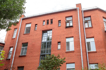 The facade of the old red brick building that was built 100 years ago against the backdrop of the White Sky. Ancient decoration of the building. Restoration of buildings. Old details. Large windows on