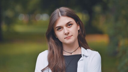 Young georgian woman with long brown hair and white shirt posing in a park, looking serene and confident