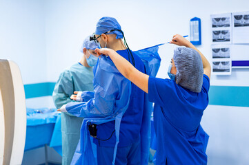 Surgery team readies in OR. Team of medical professionals get ready for surgery, wearing protective gear in a hospital operating room.