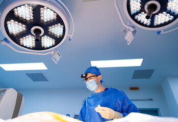 Surgeon operating in sterile room. A surgeon performs a complex operation under bright lights,...