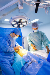 Surgeons at work in hospital. Two surgeons in surgical attire work diligently in a bright operating...