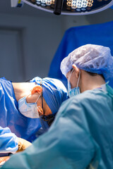 Fototapeta premium Surgeons at work in hospital. Surgeons in sterile attire focus intently during a complex procedure in a well-lit operating room.