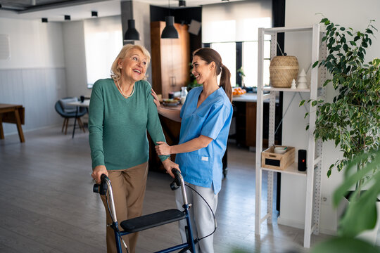 Professional Healthcare Worker Supporting Elderly Woman Using Walker During Physical Therapy Session In Contemporary Medical Center