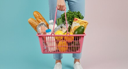 A close-up of a person carrying a modern pink wire shopping basket filled with fresh groceries.