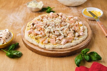 Pizza prepared for baking on yeast dough with chicken fillet, mozzarella cheese and mushrooms on a...
