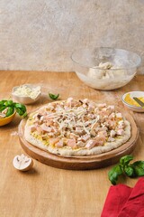 Pizza prepared for baking on yeast dough with chicken fillet, mozzarella cheese and mushrooms on a wooden board on a wooden background. Baking is savory.
