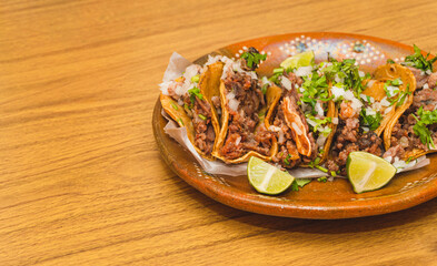 Tacos de suadero con cilantro y cebolla acompañado con limones sobre un plato de barro