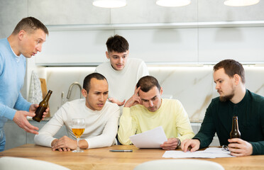 Fototapeta premium Troubled man reading legal notice surrounded by friends providing moral support sitting at table n home kitchen during informal friendly meeting..