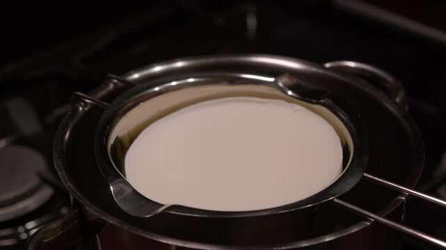 A large piece of butter or white chocolate is placed in a saucepan and placed in a water bath to begin the melting process. Close up.