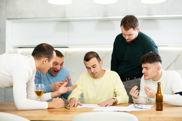 Man appearing upset as reading document, while friends gathering around, offering support and advices during friendly meeting at home kitchen..