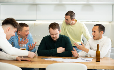 Fototapeta premium Man appearing upset as reading document, while friends gathering around, offering support and advices during friendly meeting at home kitchen..