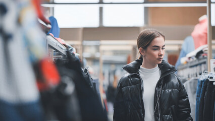 Shopper browsing clothing rack, examining trendy garments inside retail boutique with hanging...