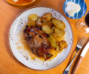Baked shank with pieces of potato dished up in a plate on the laid restaurant table