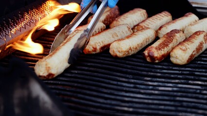 Metal tongs gripping bratwursts over sizzling flames, charring savory sausages during backyard barbecue gathering with friends enjoying summer cookout