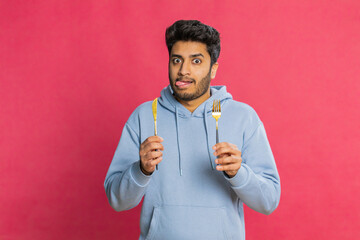 Hungry Indian man holding fork and knife, eagerly anticipating a delicious meal, licking lips with...