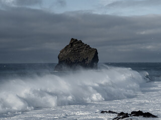 A lone sea stack rises against the Atlantic’s crashing waves at Valahnúkamöl, creating a dramatic seascape of rugged volcanic rock, powerful tides, and misty ocean spray