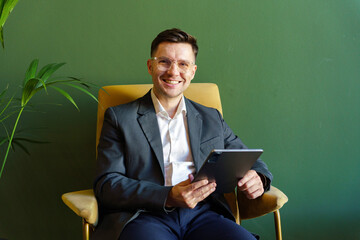 Professional man sits comfortably in a modern chair holding a tablet in a stylish green office space