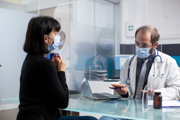 Young doctor consulting with sick woman and focusing on treatment options during clinic appointment. Male physician speaking with female patient at hospital desk and assuring safe recovery.