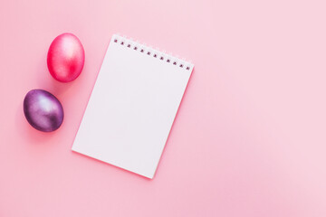 Flat lay with notebook mock up and colorful painted eggs on pink pastel background. Spring note trendy minimal holiday concept, place for text, logo, wishes. Empty space, list, mockup. Top view