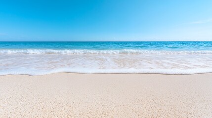 Fototapeta premium Sandy Beach with Gentle Waves Under a Clear Blue Sky for Relaxation