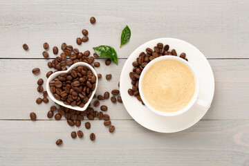 Cup of coffee with coffee beans and leaves on wooden background,top view