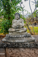 Smiling Seated Buddha Statue in Xieng Khuan Buddha Park, Vientiane, Laos Surrounded by Ornate Stonework and Lush Garden Foliage