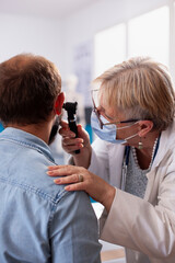 White man sits calmly in clinic room as senior ent specialist checks his ear for potential hearing...