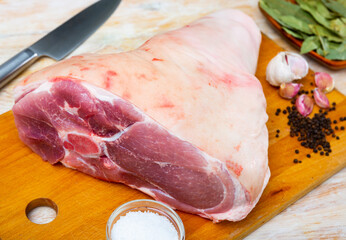 Large raw pork leg on wooden table with seasonings prepared for baking. Cooking ingredients..