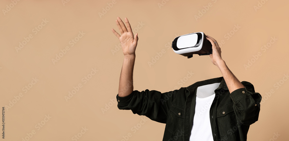 Leinwandbilder A person enjoys a virtual reality experience, wearing a headset and waving their hand. The background is a solid beige, emphasizing the focus on the user and their interaction with virtual worlds.
