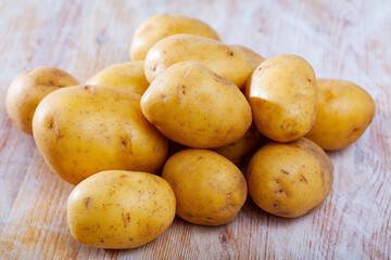 Pile of raw potatoes at wooden table in home kitchen, nobody